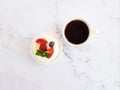 Pavlova mini cake with fruits and mint leaves and a cup with black coffee.