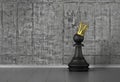 Pawn in a golden crown on concrete background.