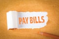 PAY BILLS concept. Text under torn paper. Orange pencil and office supplies Royalty Free Stock Photo