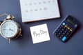 Pay day word on note with calendar, calculator and clock flat lay on blue background Royalty Free Stock Photo