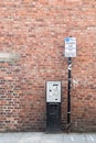 Pay and Display parking meter with information sign on a pole in front of the red brick wall Royalty Free Stock Photo