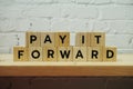 Pay It Forward alphabet letter on white brick wall and wooden shelves background Royalty Free Stock Photo