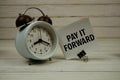 Pay It Forward text message on sticky note with alarm clcok on wooden background Royalty Free Stock Photo