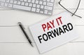 PAY IT FORWARD text on notebook with keyboard , pen glasses on white wooden background Royalty Free Stock Photo