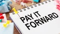 PAY IT FORWARD - text on a notepad with wrinkled paper and paper needles on wooden background Royalty Free Stock Photo