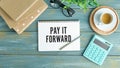 PAY IT FORWARD text on sticky on notebook with pen and glasses , blue background Royalty Free Stock Photo