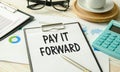 PAY IT FORWARD text on sticky on notebook with pen and glasses , wooden background