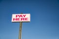 Pay Here signboard on top of an exterior wall with parked cars