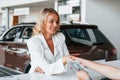 Paying for the product. Woman in formal clothes is indoors in the autosalon