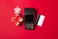 Payment terminal with credit card and gift on a red paper background. Christmas sale concept Royalty Free Stock Photo