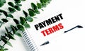 Payment terms text on spiral notebook with pen and green leaves on white background Royalty Free Stock Photo