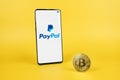 PayPal logo on smartphone and Bitcoin on yellow background