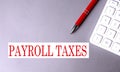 PAYROLL TAXES text written on a gray background with pen and calculator