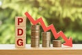 PDG text on wooden blocks with declining stack of coins and red arrow indicating decrease representing financial downturn Royalty Free Stock Photo