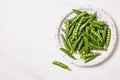 Pea pods in a white plate on a marble background. Healthy food and clean eating concept Royalty Free Stock Photo