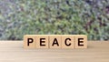 Peace word wooden cubes on table vertical over blur background with climbing green leaves, mock up, template, banner with copy Royalty Free Stock Photo