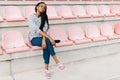 Peaceful afro-american teenager is listening to music in earphones while sitting on the pink seats on the stadium. Royalty Free Stock Photo