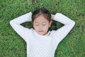 Peaceful Asian little child girl with hands behind head and closed eyes resting on green grass outdoors in summer park. Top view Royalty Free Stock Photo