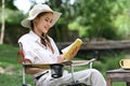 Peaceful asian woman reading book during camping alone near creek on summer holiday Royalty Free Stock Photo