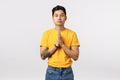 Peaceful attractive asian young man in yellow t-shirt with tattoos, hold hands in pray, palms together over chest, look Royalty Free Stock Photo