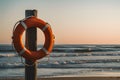 Peaceful beach scene at sunset with orange lifebuoy, wooden post, waves, and colorful sky Royalty Free Stock Photo