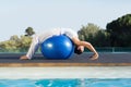 Peaceful brunette in cobra pose over exercise ball poolside