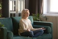 Calm senior woman meditating on couch at home