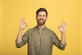 Peaceful european middle aged man with closed eyes meditating, standing isolated on yellow background, studio shot