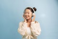 Peaceful good looking magnetic lady standing isolated over blue background, closing eyes, holding headphones, listening to music