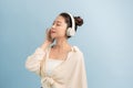 Peaceful good looking magnetic lady standing over blue background, closing eyes, holding headphones, listening to music