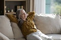 Peaceful happy sleepy elderly homeowner woman sitting on soft couch