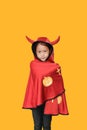 Peaceful little Asian child girl dressed Halloween costume. Kid in Dracula robe isolated on orange background