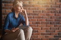 Peaceful mature blonde caucasian woman looking thoughtful, holding tablet pc while sitting in front of brick wall at