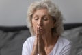 Peaceful mature woman with closed eyes praying in bedroom