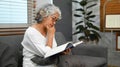 Peaceful middle age woman relaxing on couch and reading interesting book, enjoying leisure time at home Royalty Free Stock Photo