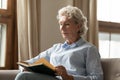 Peaceful middle aged woman reading paper book bestseller at home.