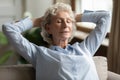 Peaceful older grandma relaxing on couch with closed eyes.