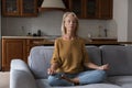 Peaceful older woman meditate seated in lotus position at home