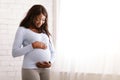 Peaceful pregnant afro woman hugging her tummy at home Royalty Free Stock Photo