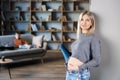 Peaceful pregnant woman touching her belly in modern interior of room and her older child sitting on couch and looking to mother. Royalty Free Stock Photo