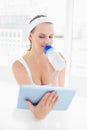 Peaceful pretty sportswoman drinking water while using tablet pc