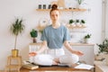 Peaceful redhead young woman is sitting with closed eyes on table in lotus position Royalty Free Stock Photo