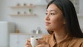 Peaceful relaxed Asian chinese japanese woman sit in kitchen hold cup of tea dreaming think feel harmony enjoy drink Royalty Free Stock Photo