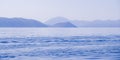 Peaceful seascape. Beautiful blue sky over calm sea with sunlight reflection. Sea waves. Mountains on horizon.