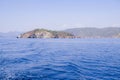 Peaceful seascape. Beautiful blue sky over calm sea with sunlight reflection. Sea waves. Mountains on horizon.