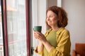 Peaceful senior woman inhaling tea aroma while standing near window at home Royalty Free Stock Photo