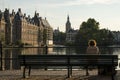 A curly lady sitting on a bench facing the early sunset at Hofvijver pond of The Hague city