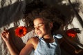 peaceful young African American girl with closed eyes lies on bed with stunning orange Gerbera flowers in the warm rays