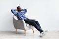 Peaceful young black man relaxing in armchair against white studio wall, free space Royalty Free Stock Photo