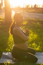 Peaceful young positive pregnant woman in gymnastic suit does yoga and meditate sitting on mat on green grass on sunny Royalty Free Stock Photo